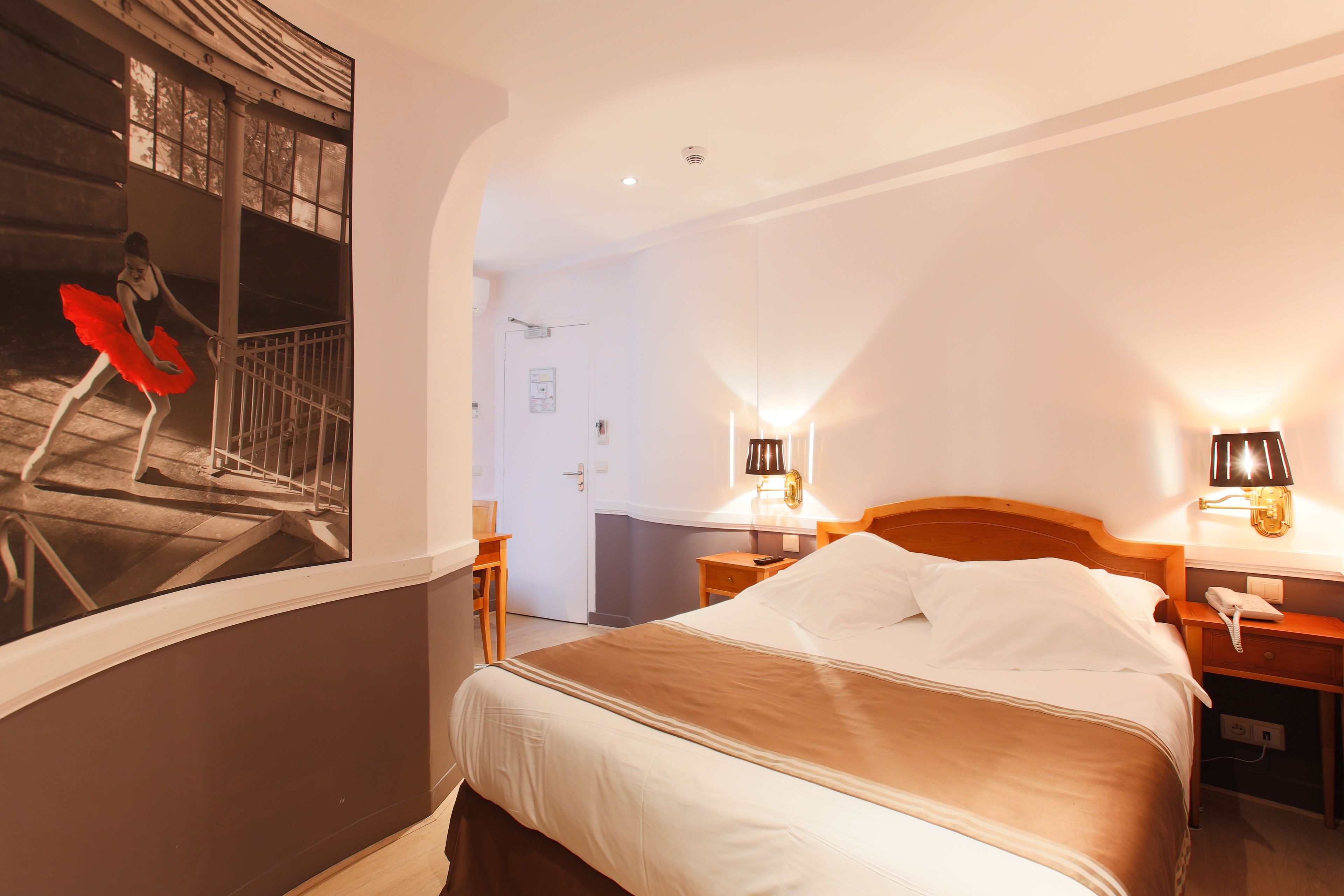 Una habitación de hotel con una cama grande, dos mesitas de noche, una lámpara de pared y una puerta que da a otra habitación.