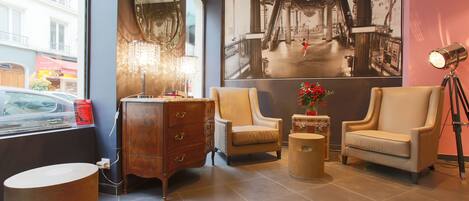Een moderne lobby met een groot raam, een vintage dressoir, twee fauteuils, een kleine tafel met een vaas en een vloerlamp.