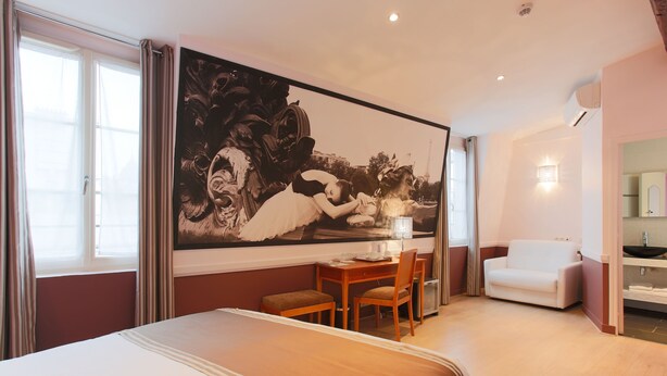 Quarto de hotel com uma cama grande, uma escrivaninha com cadeira, um sofá e um quadro grande na parede.