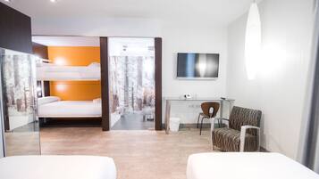 Een moderne hotelkamer met een stapelbed, een bureau met stoel, een televisie en een groot raam met uitzicht op bomen.