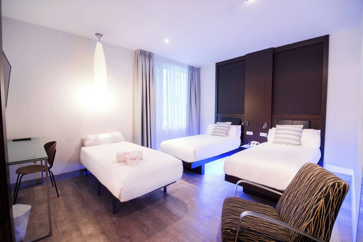 Een hotelkamer met twee bedden, een bureau, een stoel en een groot raam met gordijnen.