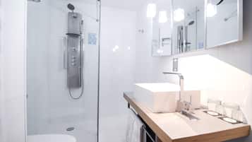 Een moderne badkamer met een douchecabine van glas, een witte wastafel en een spiegel erboven.