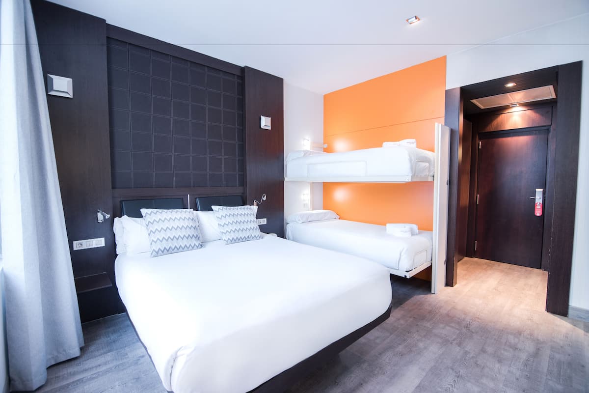 Een hotelkamer met een groot bed, een tweede stapelbed, een donker houten hoofdeinde en een oranje accentmuur.