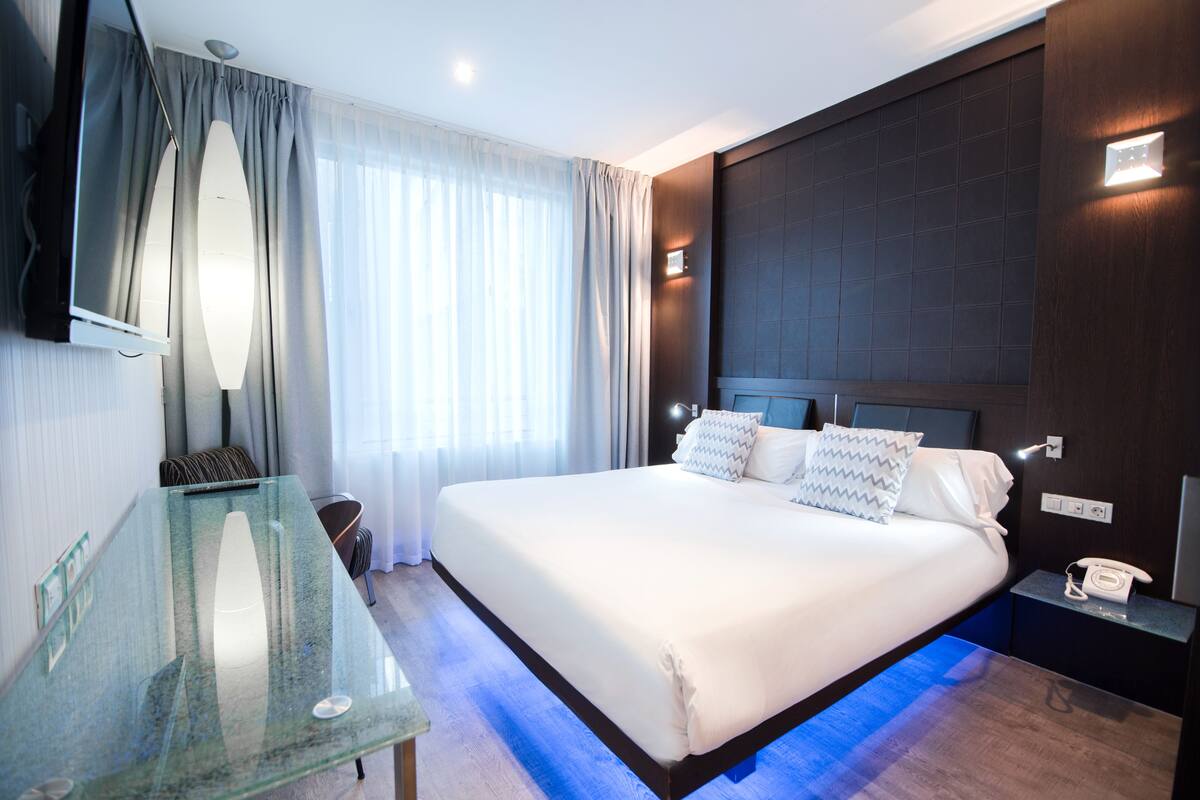 Een moderne hotelkamer met een groot bed, een glazen tafel, een televisie en een bedtafeltelefoon.