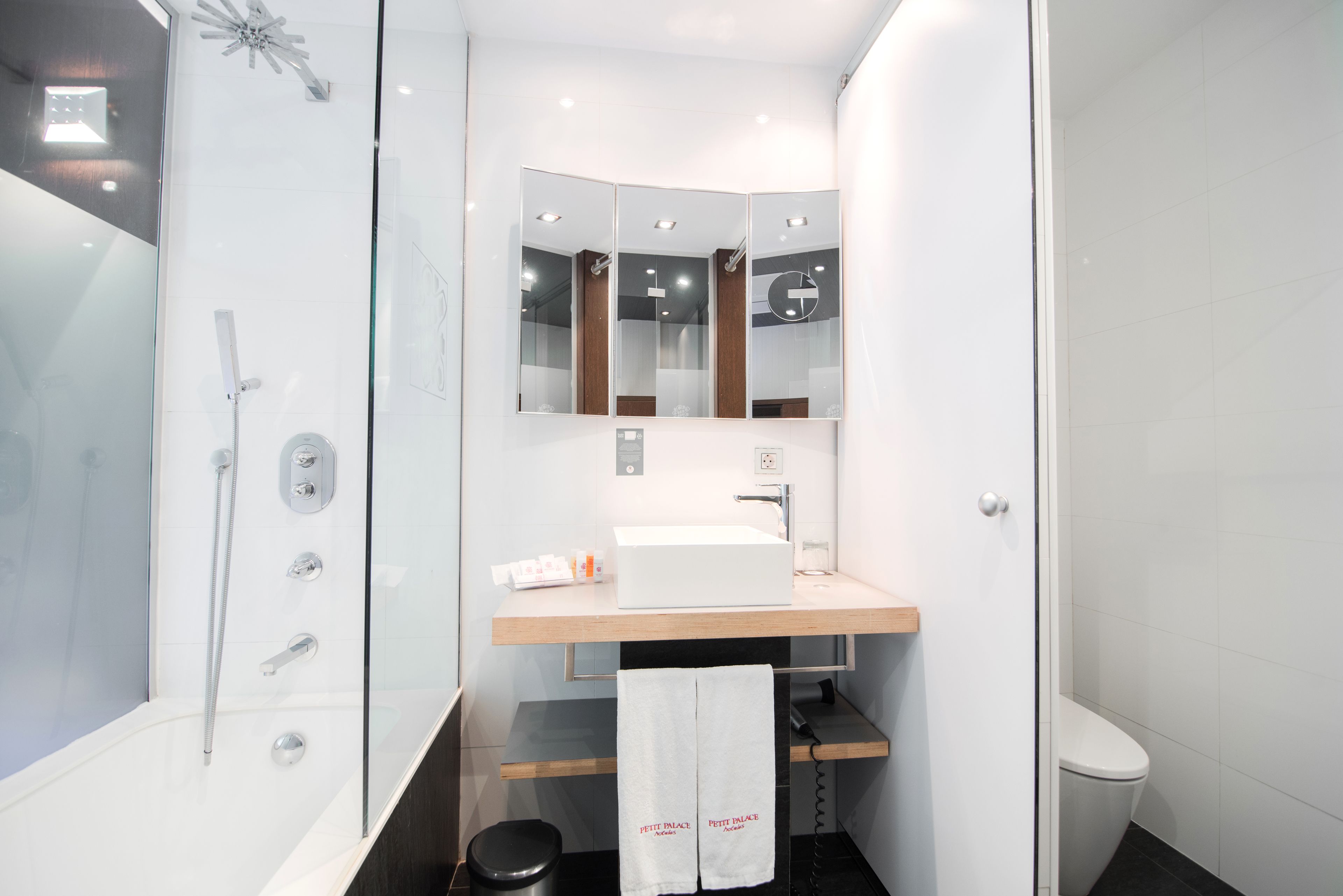 Un baño moderno con ducha envuelta en vidrio, tocador de madera con lavabo y un espejo sobre el tocador.