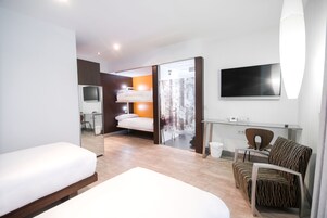 Una habitación de hotel moderna con una cama, un escritorio con una silla, un televisor y una puerta corredera que da a un baño.