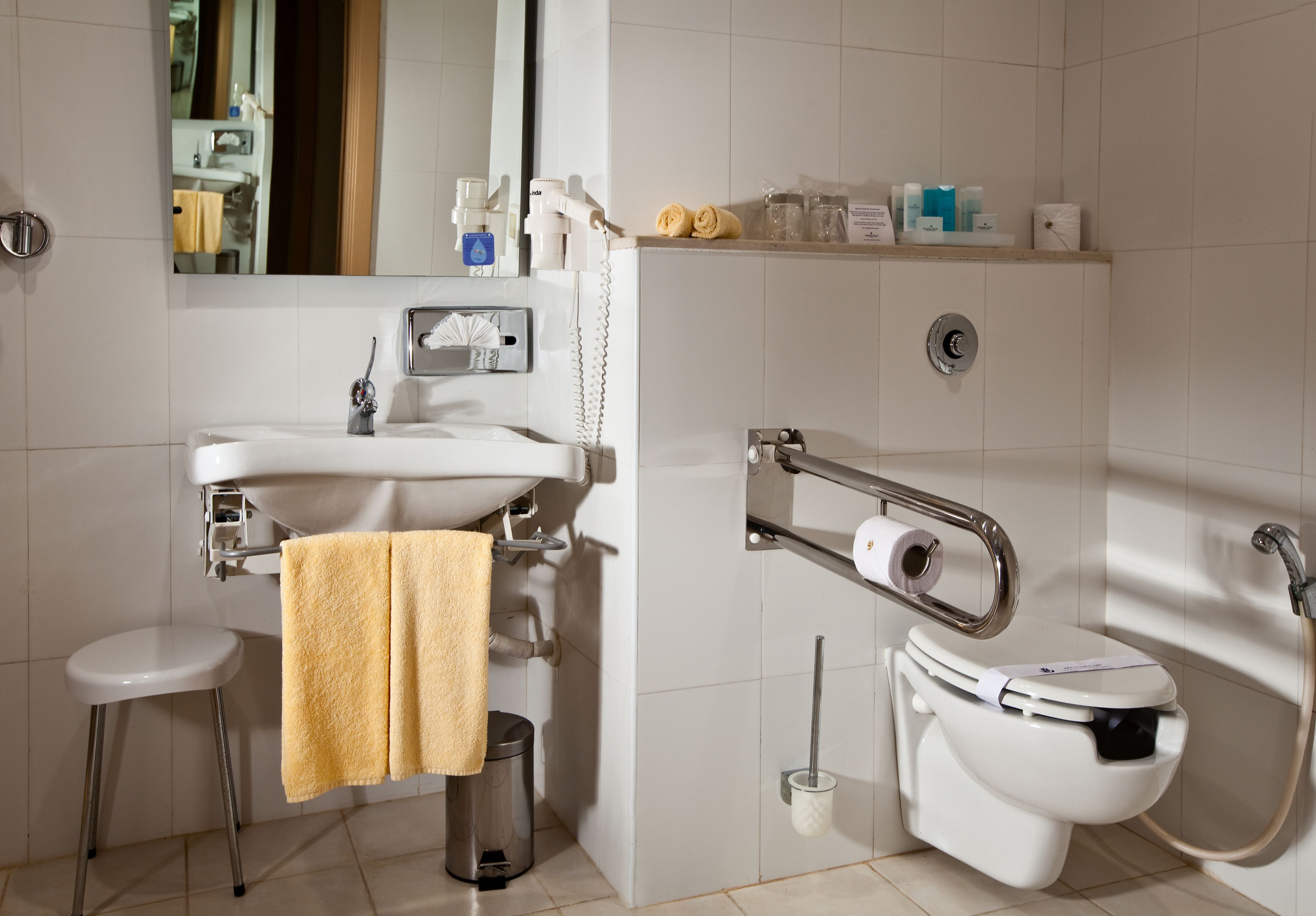 A modern bathroom with a sink, toilet, and bidet, featuring a towel rack and a mirror.