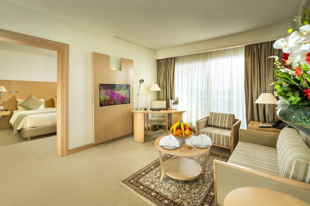 Quarto de hotel com cama, sofá, mesa de jantar com frutas e um quadro na parede.