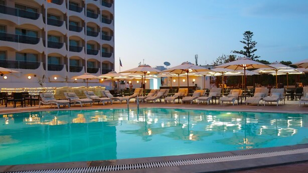 A pool area with lounge chairs and umbrellas, surrounded by a building with balconies.