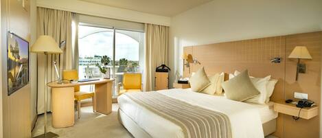 A hotel room with a large bed, a desk, a chair, and a view of the city through the window.