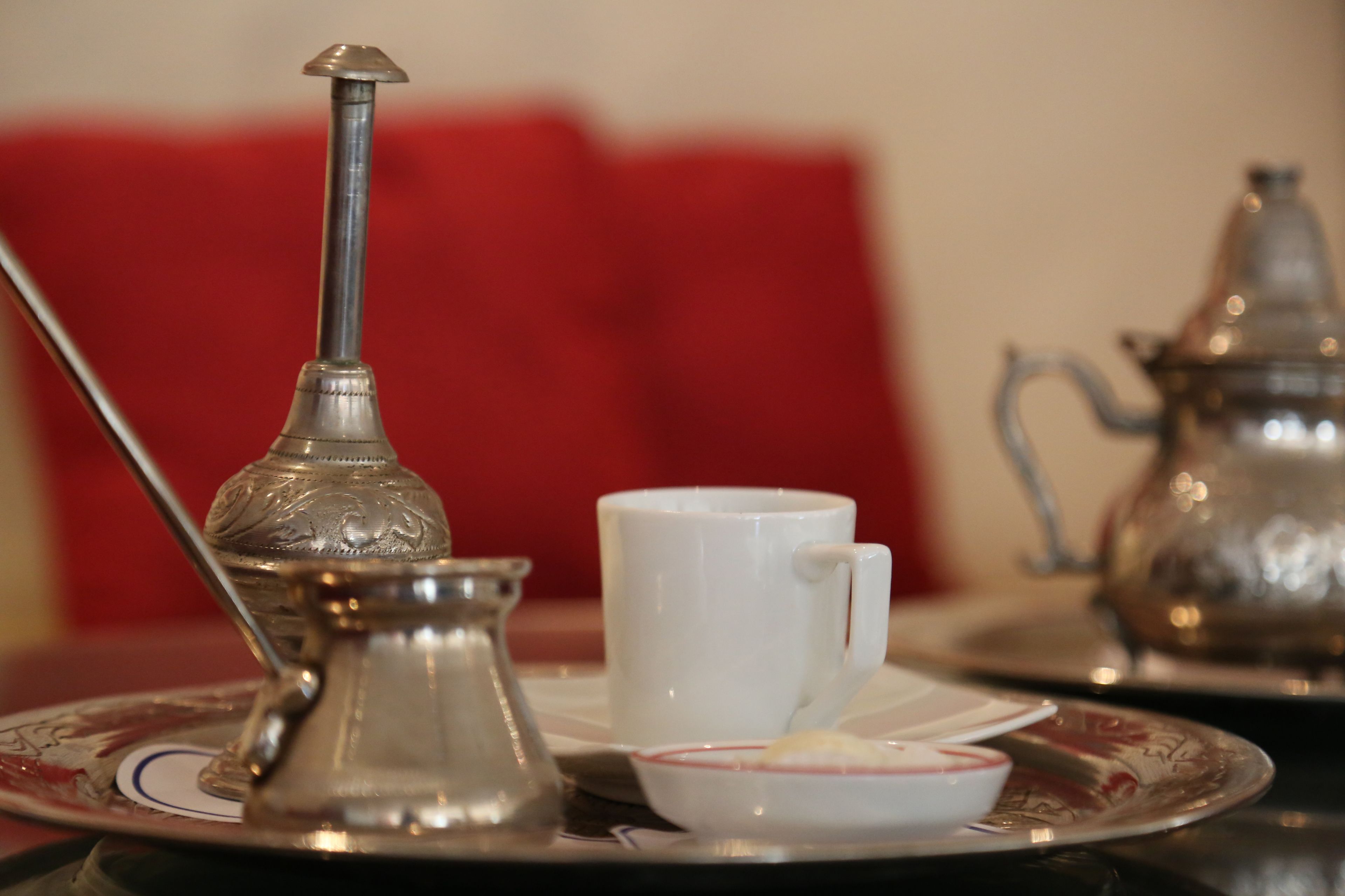 A table with a traditional silver teapot, a white cup, and a small bowl with a red rim.