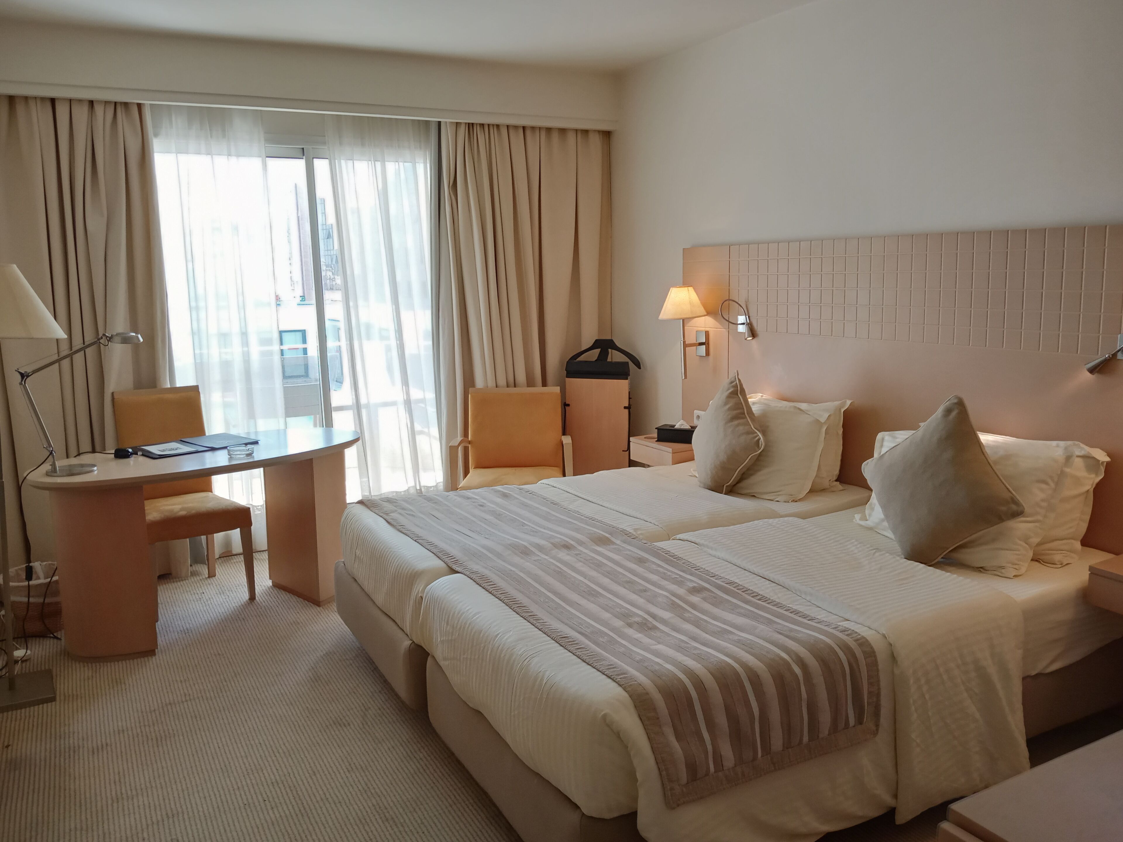 A hotel room with a large bed, a desk, a chair, a nightstand, and a lamp.