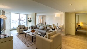 A modern hotel room with a large window, a sofa set, a coffee table, and a desk area.