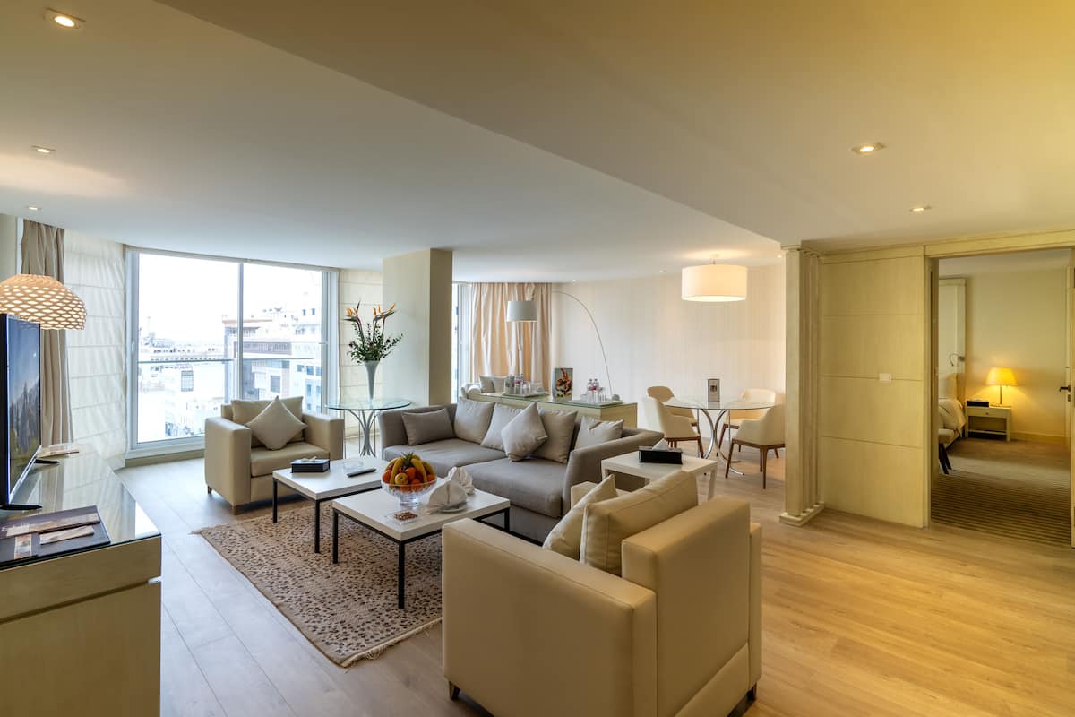 Quarto de hotel moderno com uma janela grande, um conjunto de sofás, uma mesa de centro e uma área de trabalho.
