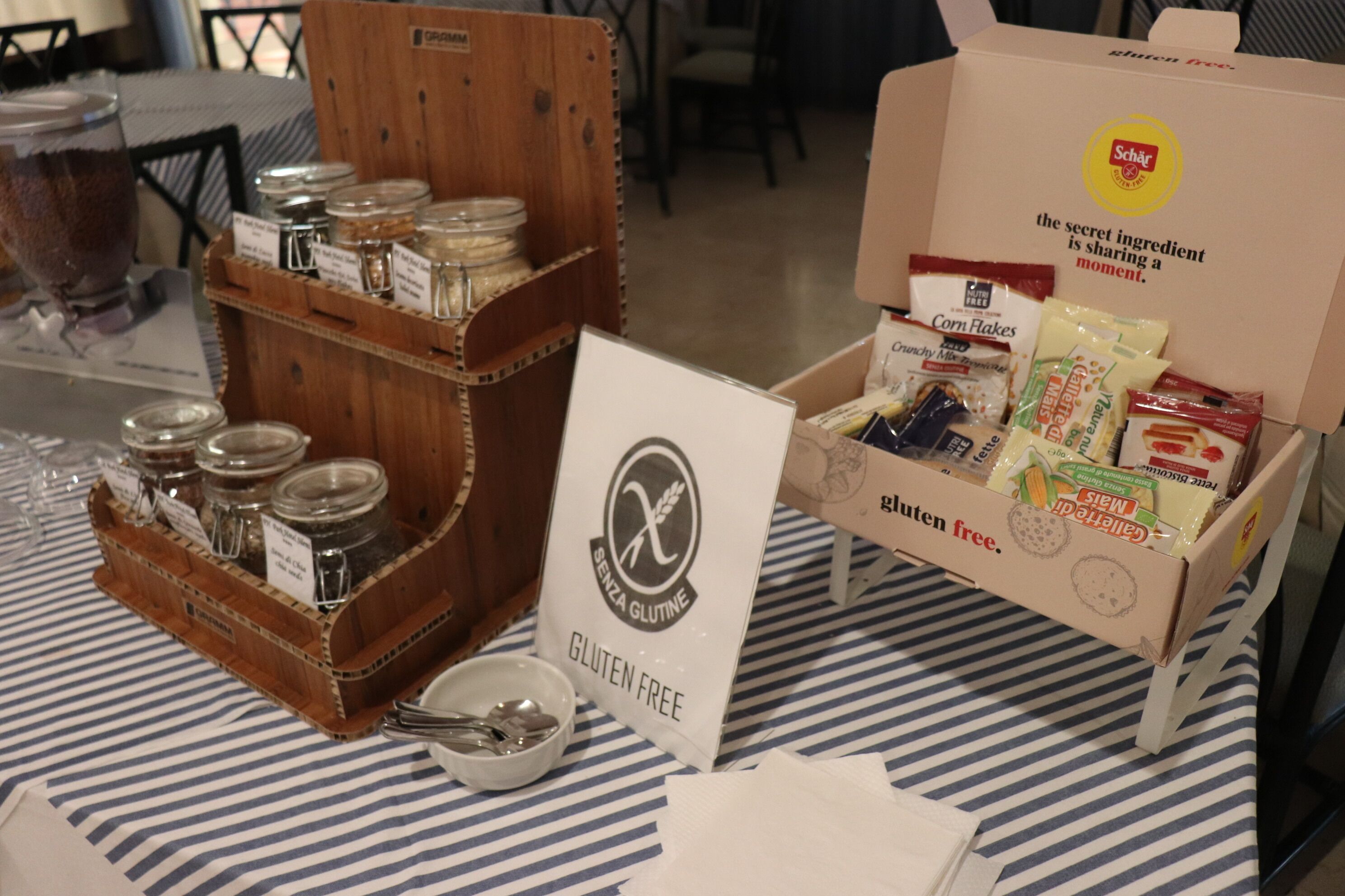 Una mesa con un cartel que indica opción sin gluten, una caja de productos sin gluten y un cesto de madera con frascos.