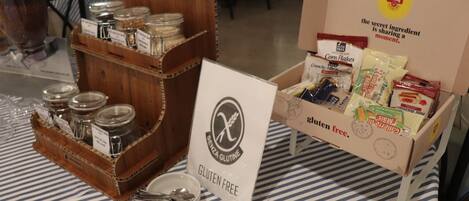 Una mesa con un cartel que indica opción sin gluten, una caja de productos sin gluten y un cesto de madera con frascos.
