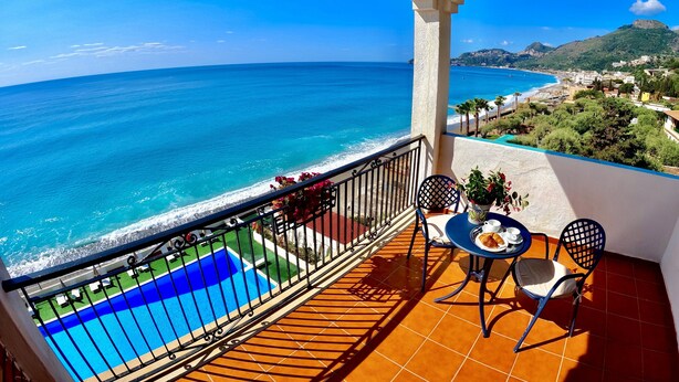 A balcony with a view of the sea, a pool, and a table with chairs. - Park Hotel Silemi (Letojanni)