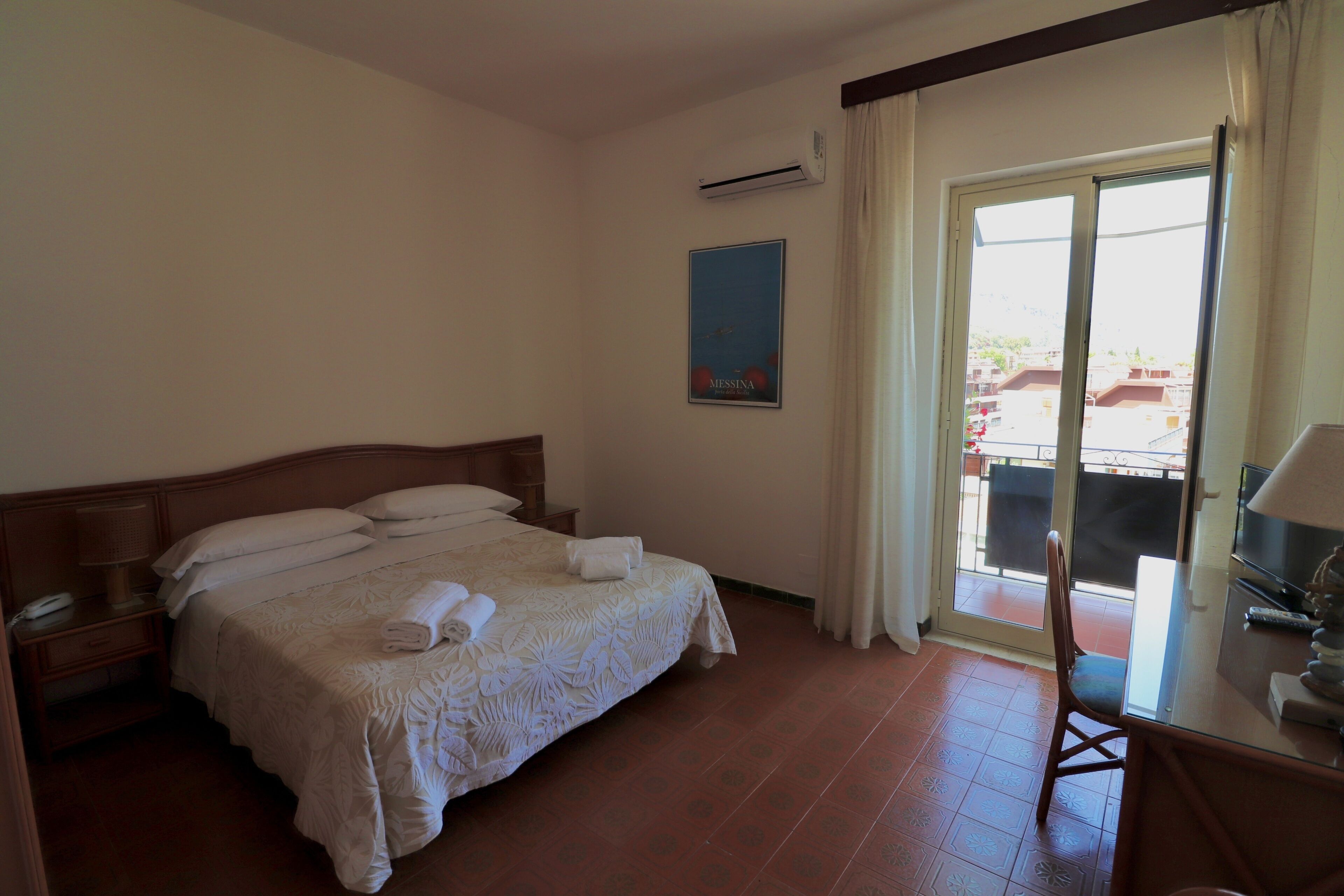 Habitación de hotel con cama, escritorio, silla y vistas al exterior.