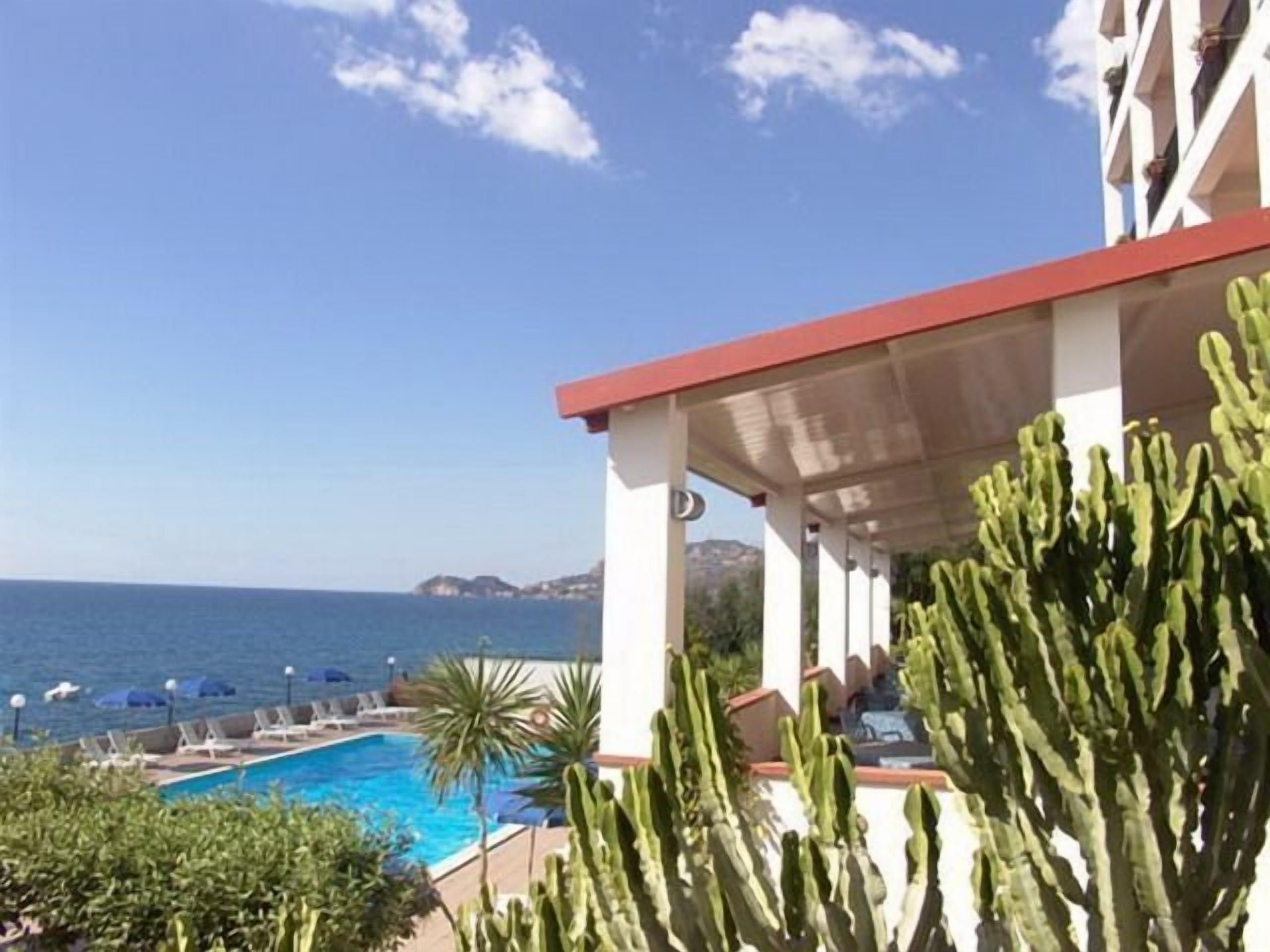 Un espace aménagé au bord de la piscine avec vue sur la mer, un patio couvert agrémenté de cactus et des chaises longues.