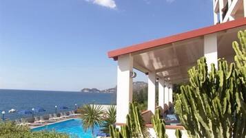 Un espace aménagé au bord de la piscine avec vue sur la mer, un patio couvert agrémenté de cactus et des chaises longues.