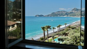 A coastal view from a window, including a beach, ocean, and distant hills. - Park Hotel Silemi (Letojanni)