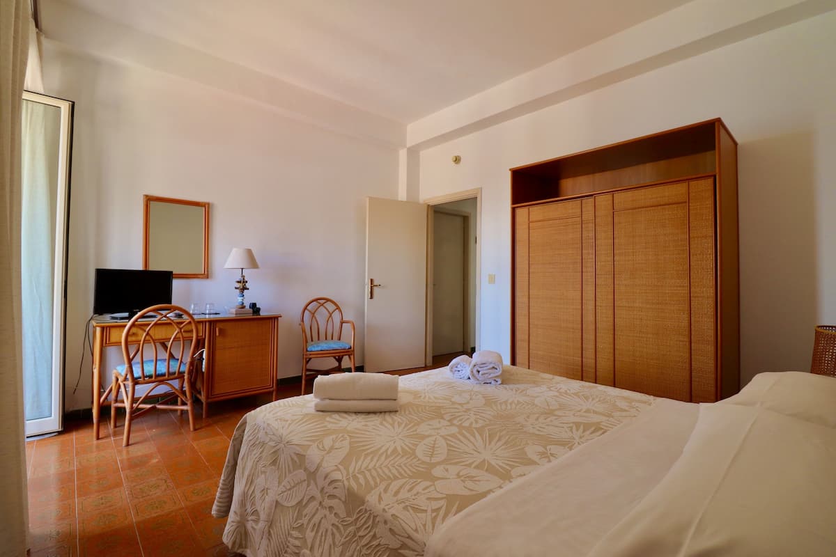 Ein Hotelzimmer mit Bett, Schreibtisch mit Computer, Stuhl, Kleiderschrank und einer Tür zu einem anderen Raum.