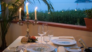 A table set for dining with candles, glasses, and plates, overlooking a body of water. - Park Hotel Silemi (Letojanni)