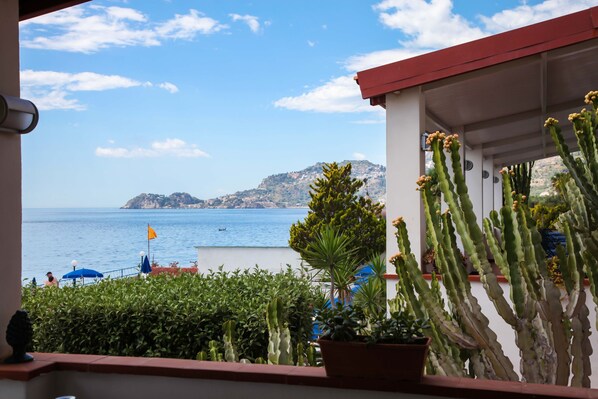 Un balcón con vista al mar, cactus y una bandera.