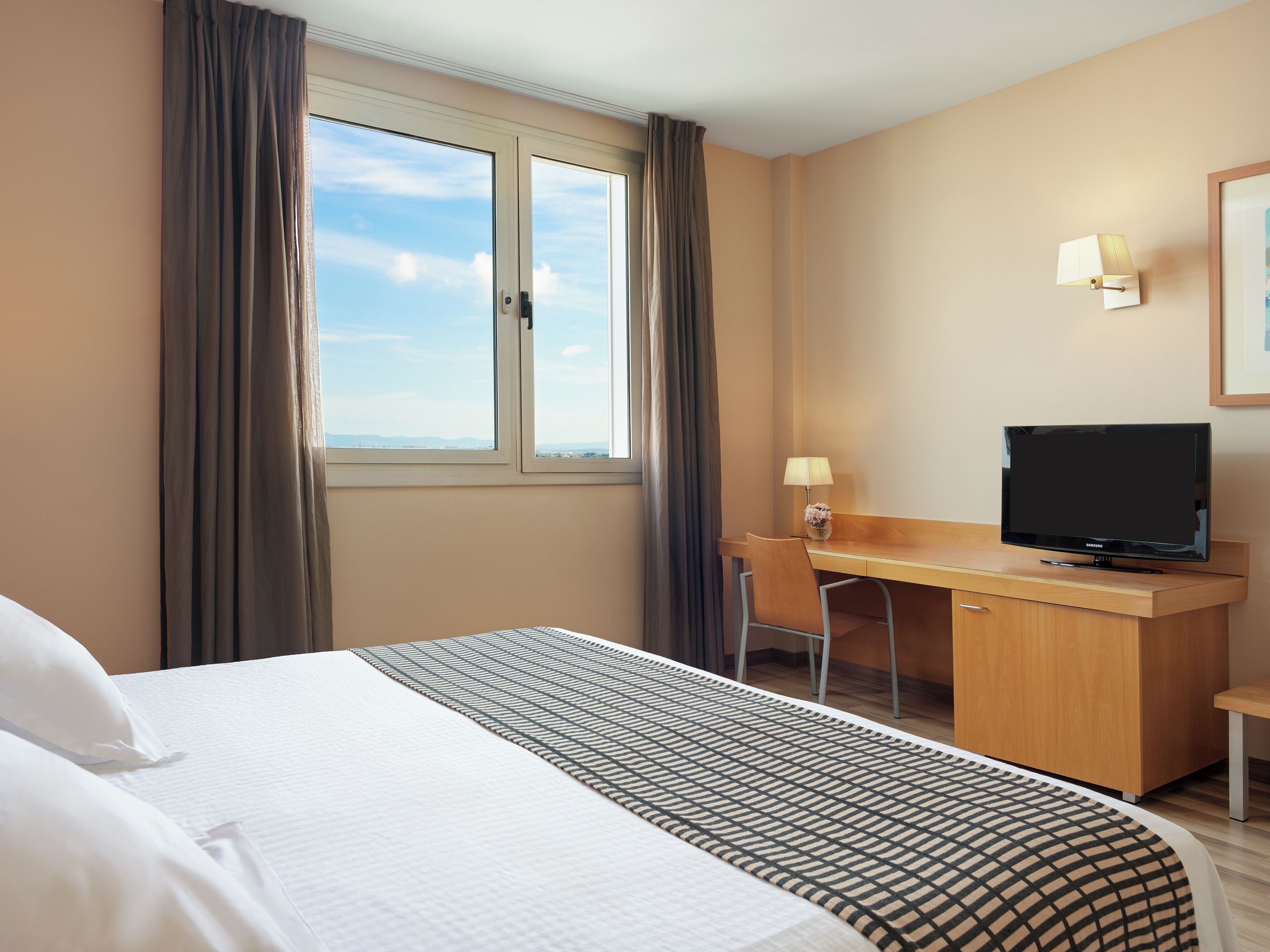 Une chambre d’hôtel équipée d’un lit, d’un bureau, d’une chaise, d’une télévision et d’une fenêtre avec des rideaux.
