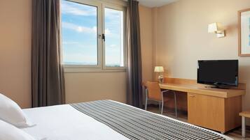Une chambre d’hôtel équipée d’un lit, d’un bureau, d’une chaise, d’une télévision et d’une fenêtre avec des rideaux.