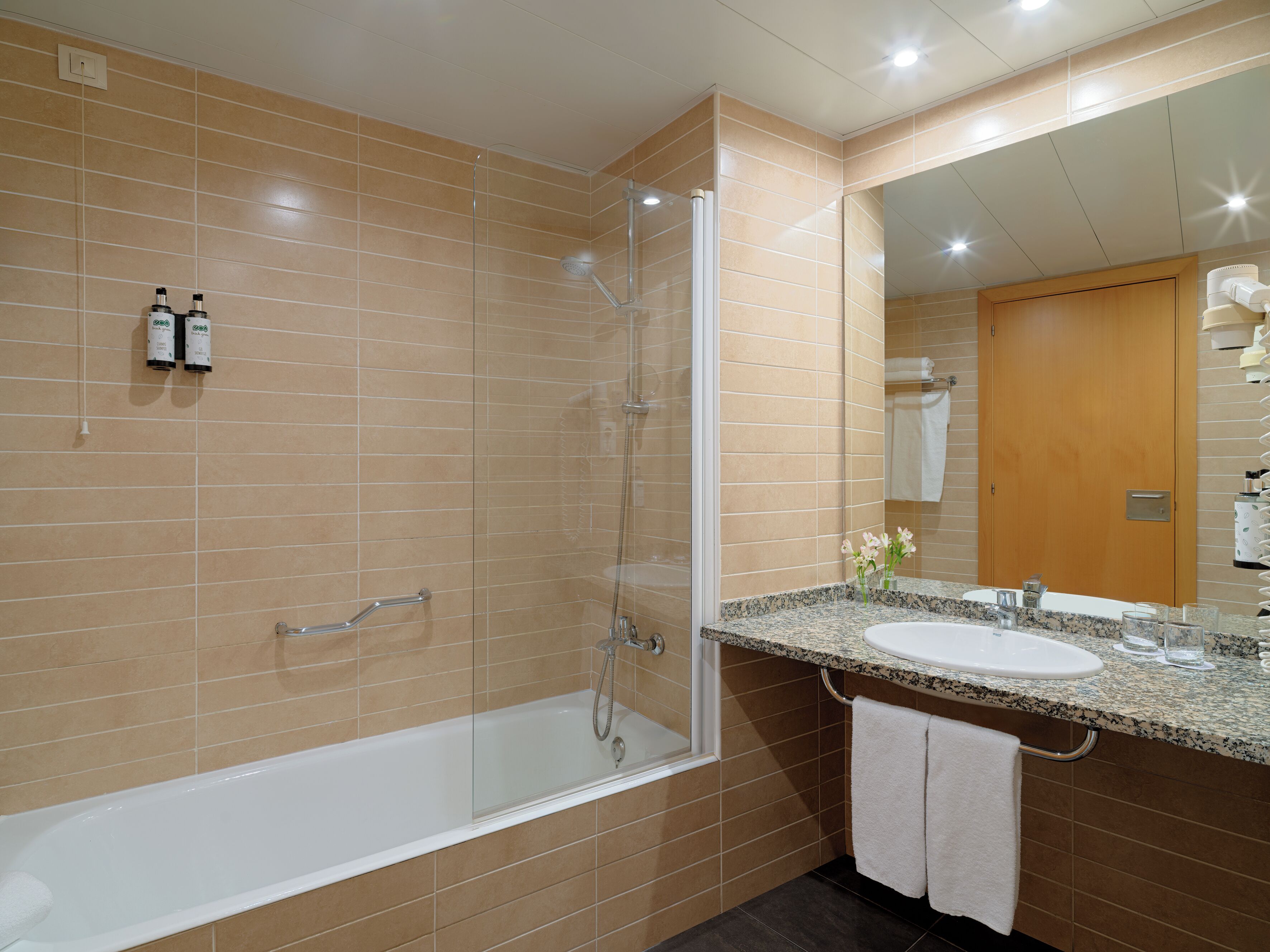 A modern bathroom with a glass-enclosed shower, a white bathtub, and a granite countertop sink.