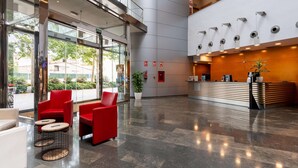Een moderne lobby met een receptiebalie, rode zitplaatsen en een grote glazen ingang.