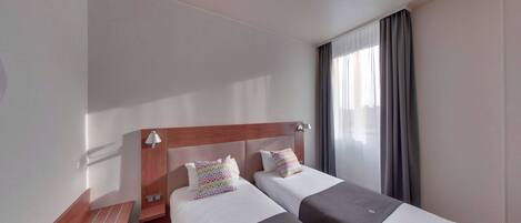 A hotel room with two beds, a wooden headboard, a bench, and a window with curtains.