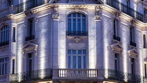Un edificio histórico con balcones ornamentales, amplias ventanas y una entrada a pie de calle con tiendas.