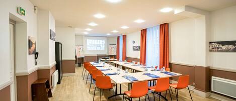 A conference room with a long table, orange chairs, and a projector screen.