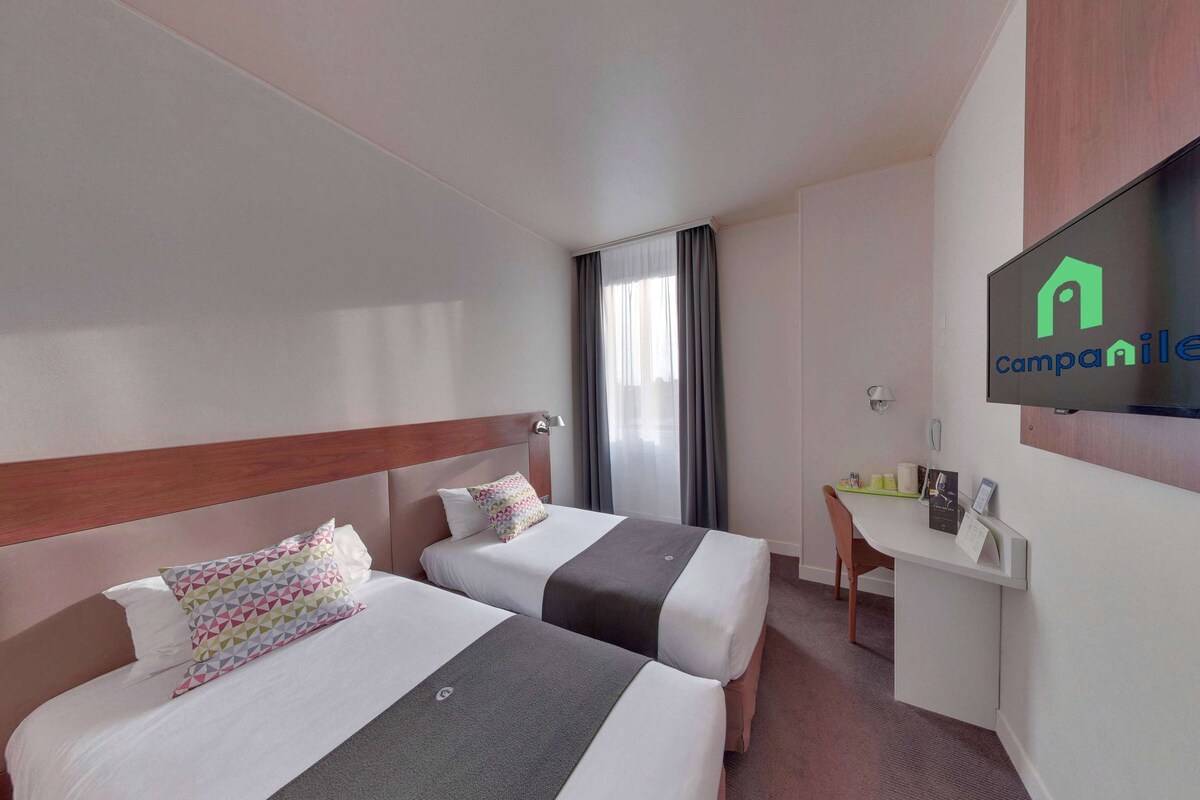 Een hotelkamer met twee bedden, een bureau, een televisie en een raam met gordijnen.