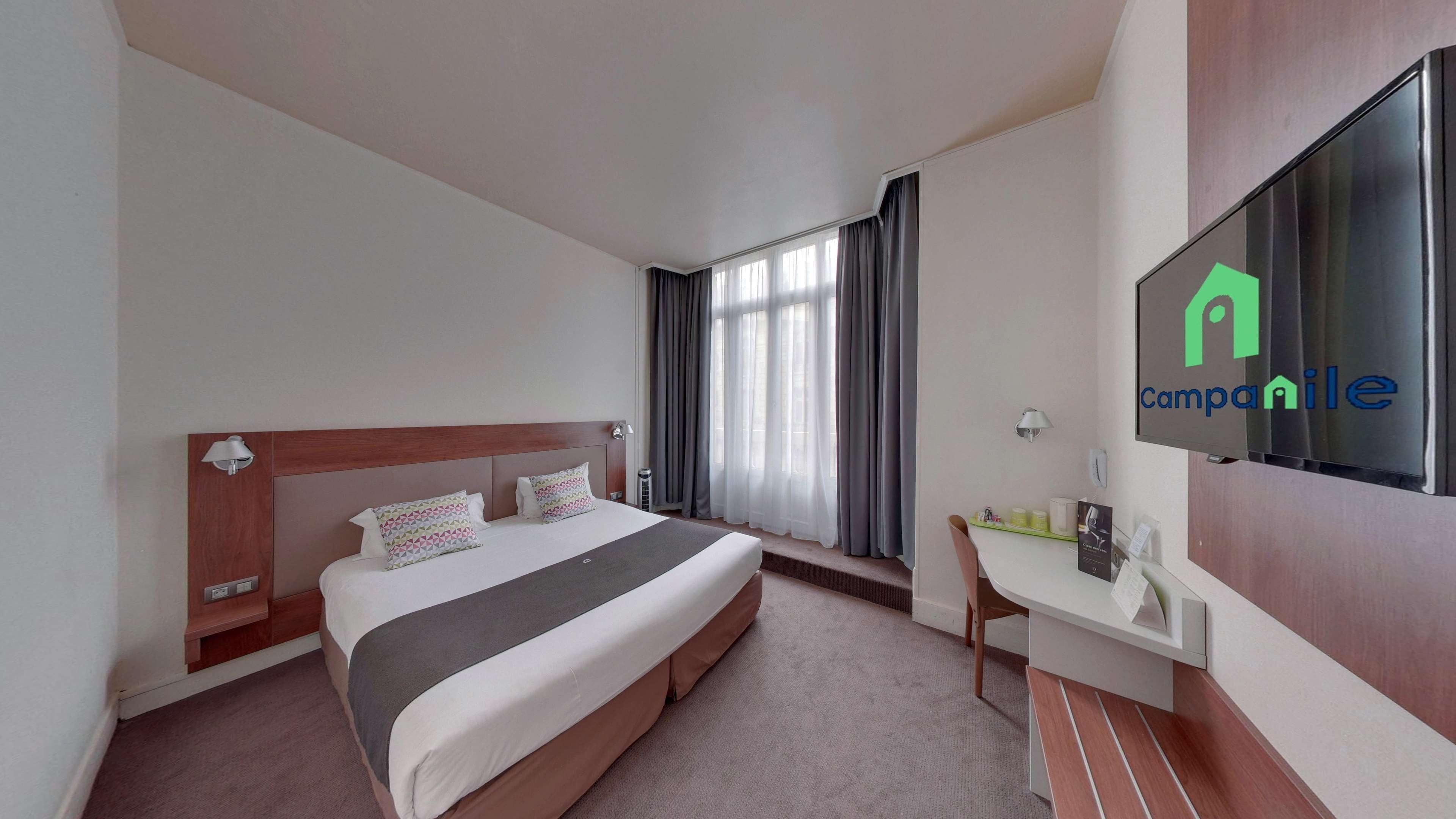 Une chambre d’hôtel avec un lit, un bureau, une chaise, une télévision et une fenêtre avec des rideaux.
