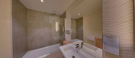 Un baño moderno con bañera, lavamanos y ducha con mampara de vidrio.