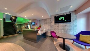 Un moderno vestíbulo de hotel con mostrador de recepción, televisor de pantalla plana, escalera y zonas de estar.