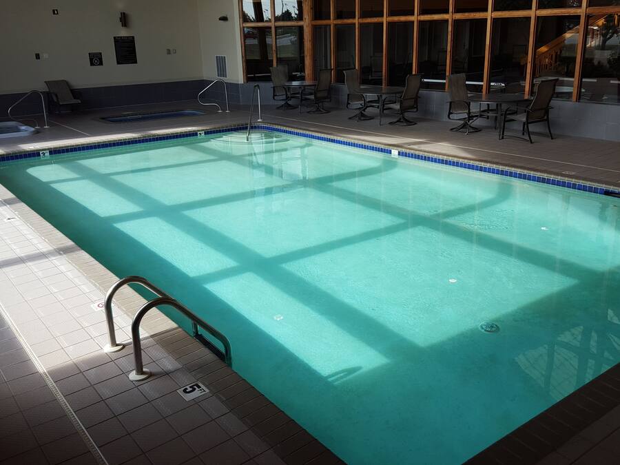 An indoor swimming pool with clear water, a diving board, and a seating area with tables and chairs.