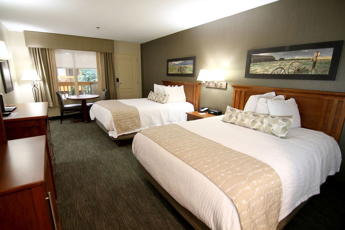 A hotel room with two beds, a desk, a chair, a lamp, and a painting on the wall.
