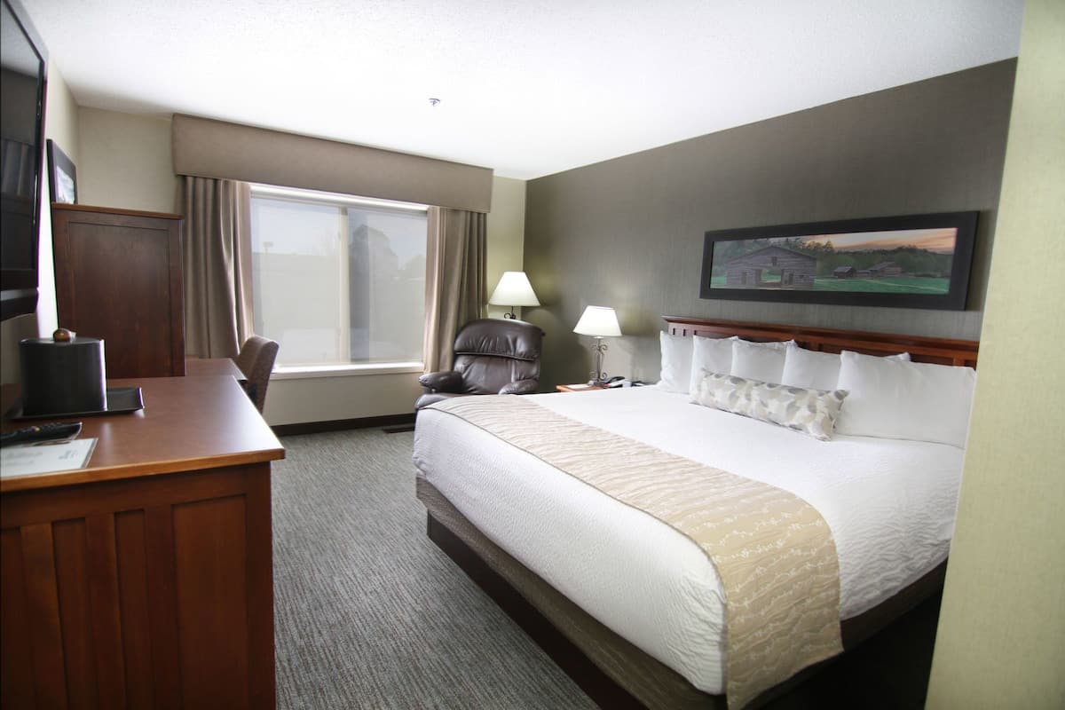 A hotel room with a large bed, a desk with a chair, a television, and a window with curtains.
