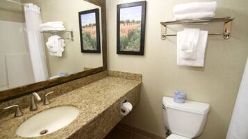 A bathroom with a granite countertop sink, a toilet, a shower curtain, and two framed pictures on the wall.