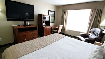 Une chambre d’hôtel dotée d’un grand lit, d’une télévision à écran plat, d’un bureau avec une chaise, d’un four à micro-ondes et d’une machine à café.