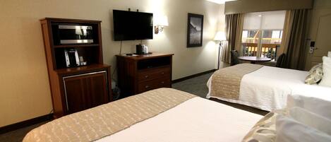 A hotel room with two beds, a TV, a desk with a coffee maker, and a window with curtains.