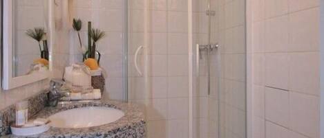 A bathroom with a curved shower enclosure, a granite countertop sink, and a trash bin.