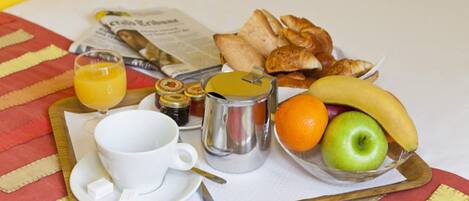 Bandeja de desayuno con cruasanes, una banana, una manzana, una naranja, una taza de café, un vaso de jugo de naranja y un periódico.