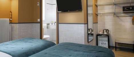 Habitación de hotel con dos camas, televisión, espejo, repisa con artículos de aseo y una mesita con tetera.