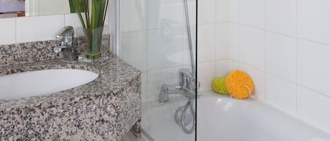 A modern bathroom with a glass-enclosed shower, a granite countertop sink, and a white bathtub.