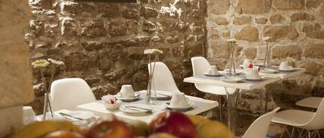 A dining area with stone walls and white chairs. Tables are set with plates, cups, and cutlery.